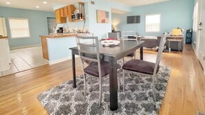 A modern kitchen with wooden cabinets, a dining area with a table and chairs, and a living space with a sofa and a TV. - The Bliss Lodge - Large House (Columbus)
