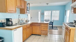 A kitchen with wooden cabinets, a dishwasher, a coffee maker, and a window with blinds. - The Bliss Lodge - Large House (Columbus)