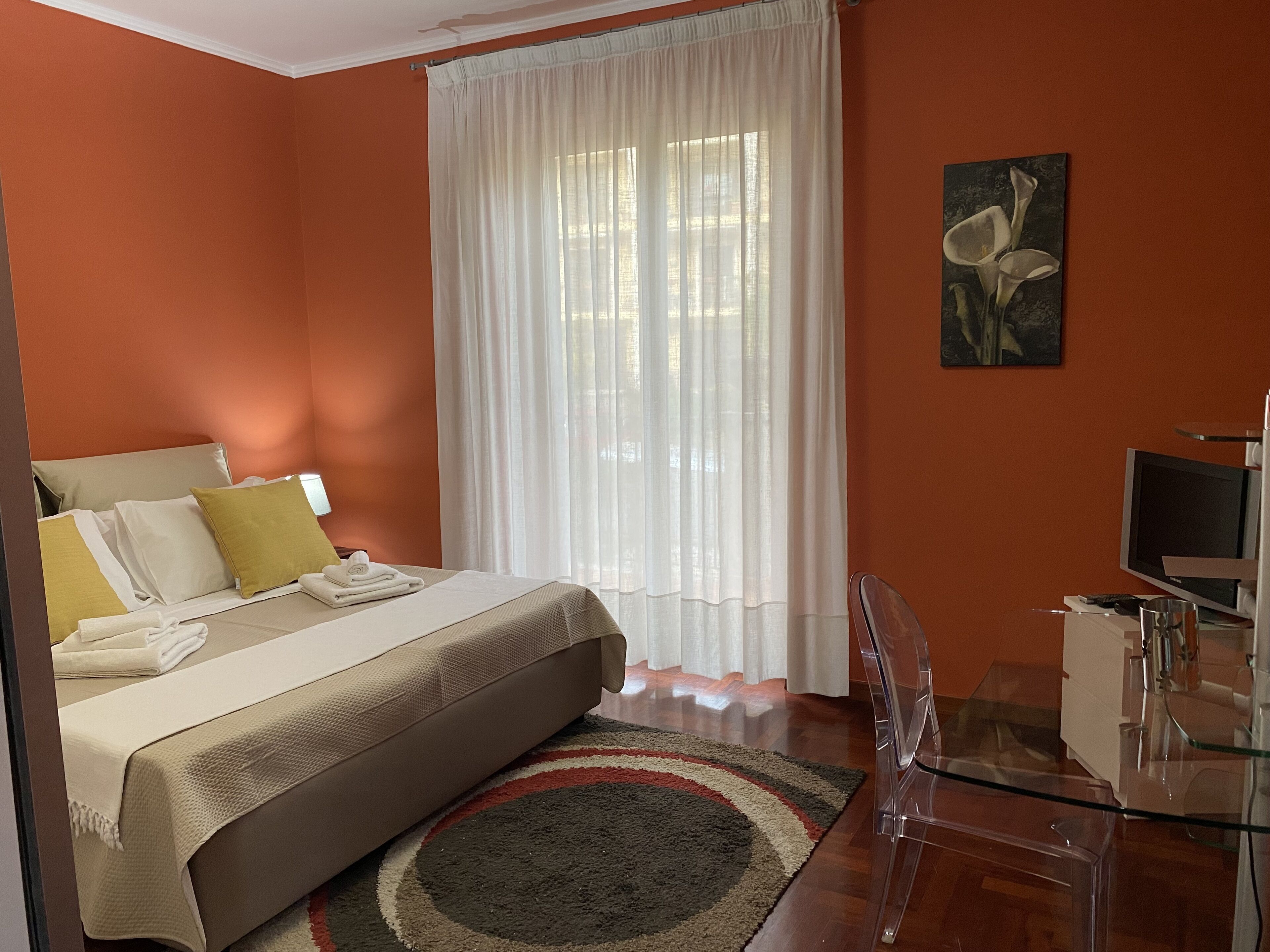 A hotel room with a bed, a desk, a chair, a television, and a painting on the wall.