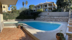 Ein Pool mit Steinmauer und Topfpflanzen, umgeben von einer gefliesten Terrasse.