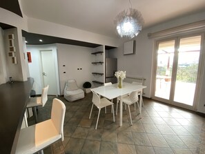 A modern kitchen with white cabinetry, a dining area with a white table and chairs, and a large window with a view of greenery.