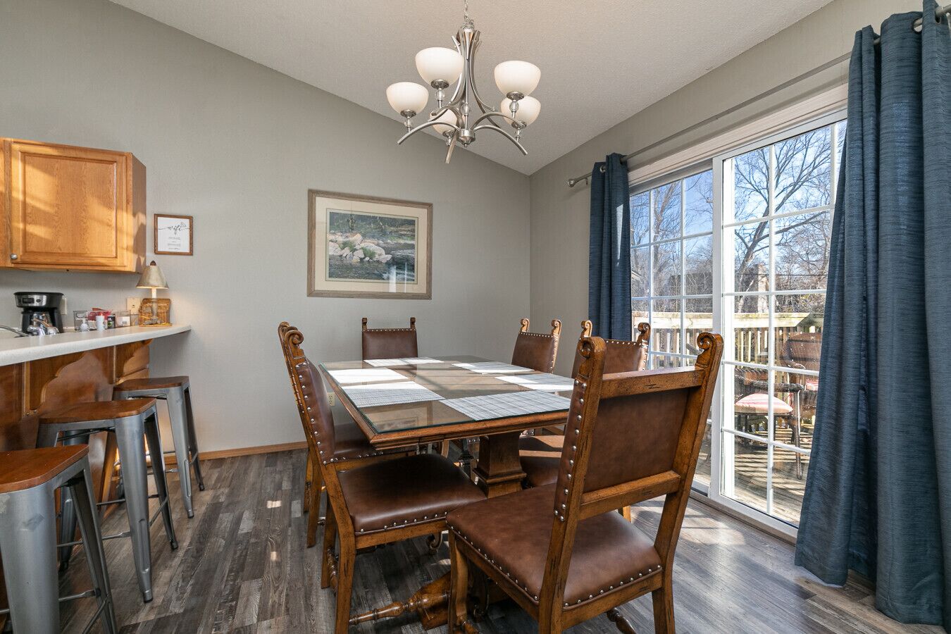 Un coin repas avec une table à plateau de verre, des chaises en bois, un lustre et une vue sur l’extérieur grâce à une grande fenêtre.