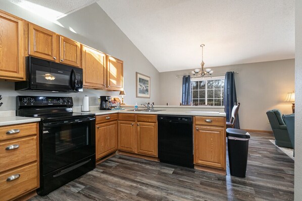 A kitchen with wooden cabinets, a black stove, a dishwasher, and a window with curtains.