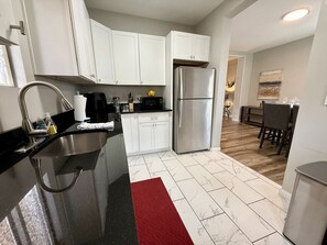 A modern kitchen with white cabinets, a stainless steel refrigerator, and a black countertop.