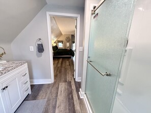 A narrow hallway with a white vanity, a glass door, and a bedroom visible in the background.