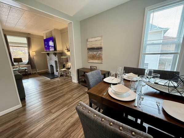 A dining area with a wooden table set for four, a fireplace, and a television in the background.