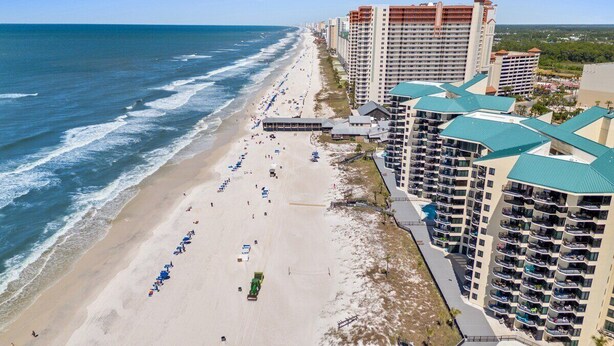 A beachfront hotel with multiple buildings, a sandy beach, and a clear view of the ocean.