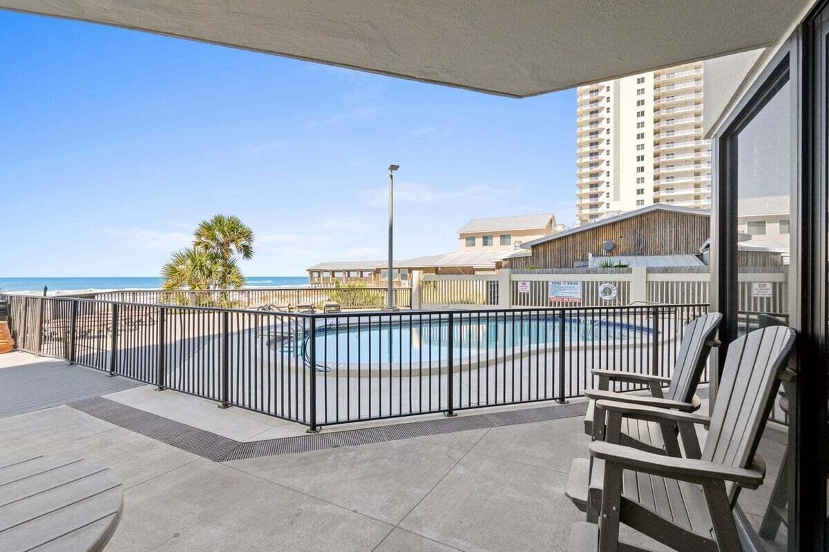 A balcony with a pool, chairs, and a view of the ocean and buildings.