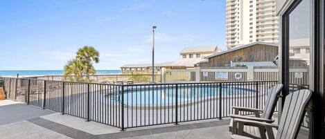 A balcony with a pool, chairs, and a view of the ocean and buildings.