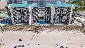 A high-rise hotel with a central pool, multiple balconies, and a beach area in the foreground.