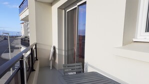 A balcony with a table and chairs, a glass door, and a view of the street. - 43 m² apartment with balcony, 80 m from Demoiselles beach, (Saint-Hilaire-de-Riez)