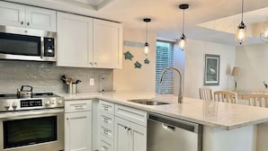 A modern kitchen with stainless steel appliances, white cabinetry, and a central island with a dishwasher. - Luxury Villa Steps to Beach & Marina Hilton Head (Hilton Head Island)