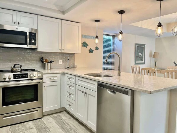 A modern kitchen with stainless steel appliances, white cabinetry, and a central island with a dishwasher.