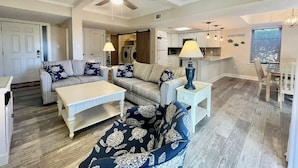 A spacious living area with a sofa, coffee table, and a dining table. A ceiling fan and kitchen are visible in the background. - Luxury Villa Steps to Beach & Marina Hilton Head (Hilton Head Island)
