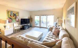 En stue med sofa, tv og et stort vindue.