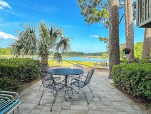 A patio with a round table and chairs, surrounded by trees and a view of a lake.