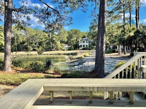 A wooden deck overlooking a pond with trees and a house in the background.