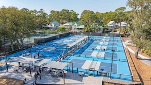 A large outdoor swimming pool area with multiple lanes, surrounded by trees and residential buildings.