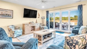 A living room with a flat-screen TV, a sofa, a coffee table, and a view through a glass door to an outdoor patio.