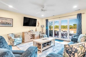 A living room with a flat-screen TV, a sofa, a coffee table, and a view through a glass door to an outdoor patio.
