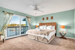 A bedroom with a bed, a ceiling fan, a nightstand with a lamp, and a view of the outdoors through a sliding door.