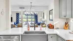 A modern kitchen with a central island, a built-in dishwasher, and a dining area with blue curtains.