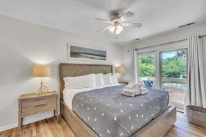 Una camera da letto con un letto, lampade sui comodini, una ventola a soffitto, una finestra con tende e un quadro al muro.