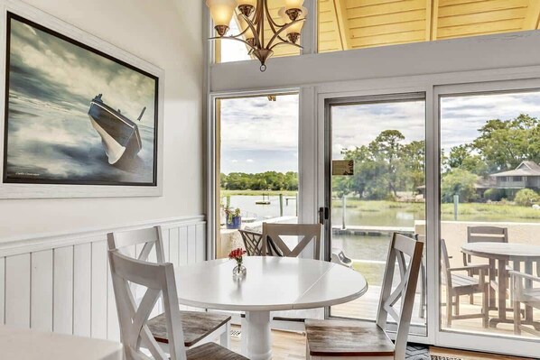 A dining area with a round table, white chairs, and a painting of a boat on the wall.