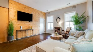 A living room with a wooden accent wall, a flat-screen TV, a sofa, a coffee table, and a potted plant. - ⭐Southern Charmer•Historic Downtown•Private Porch⭐ (Savannah)