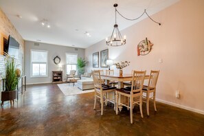 A spacious living room with a dining area, large windows, and a chandelier.