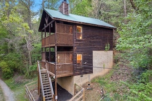 A wooden cabin with a balcony, a staircase, and a view of the surrounding forest.