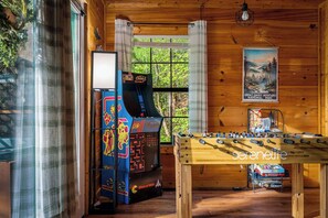 Una habitación con paredes de madera, una mesa de fútbol de mesa, un juego de arcade retro y un cartel del Parque Nacional de las Montañas Humeantes.