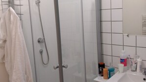 Ein modernes Badezimmer mit Duschkabine aus Glas, weißen Fliesen und einem Waschbecken mit Pflegeprodukten.