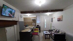 Ein kompakter Wohnraum mit Küchenzeile, einem Essbereich mit Tisch und Stühlen, einer Couch und einem an der Wand befestigten Fernseher.