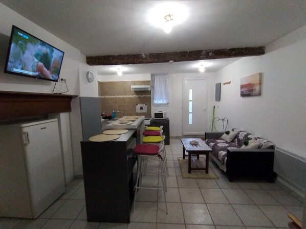 Un espacio habitable compacto con kitchenette, una zona de comedor con mesa y sillas, un sofá y un televisor montado en la pared.
