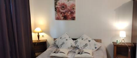 A neatly made bed with a motivational print, two bedside lamps, a wall-mounted flower painting, and a dark curtain.