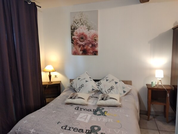 A neatly made bed with a floral print bedspread and pillows with the word "love" on them. There are two bedside lamps and a wall art piece above the bed.