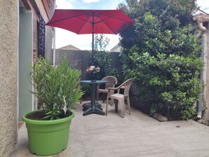 A patio area with a green potted plant, a table with two chairs, and a red umbrella.