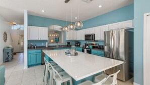 Una cocina moderna con una isla grande, armarios blancos, electrodomésticos de acero inoxidable y detalles en color turquesa.