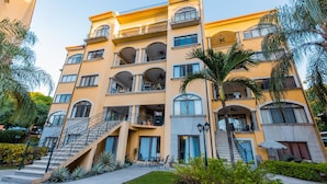Un hôtel à plusieurs étages doté de balcons, d’un escalier et d’un palmier dans la cour.