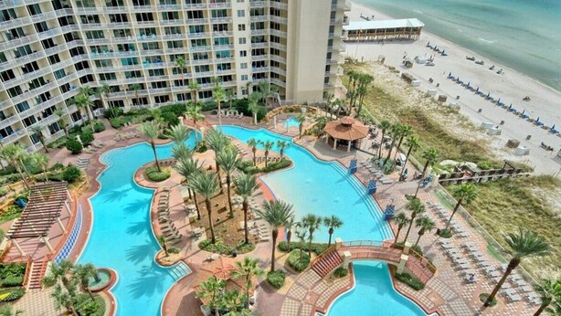 Un hotel con varias piscinas, palmeras y una zona de playa.