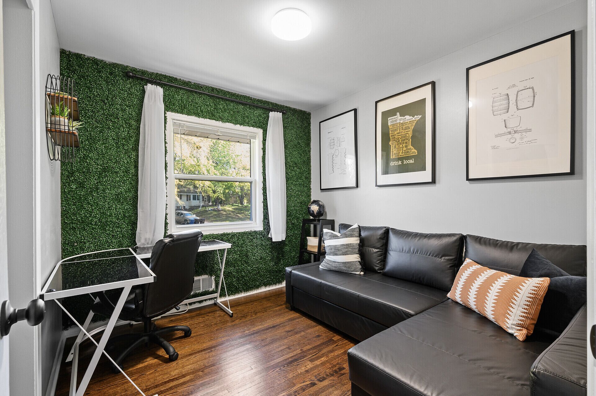 Ein modernes Zimmer mit grüner Wand, einem schwarzen Ledersofa, einem Schreibtisch mit Stuhl und gerahmten Kunstwerken an der Wand.