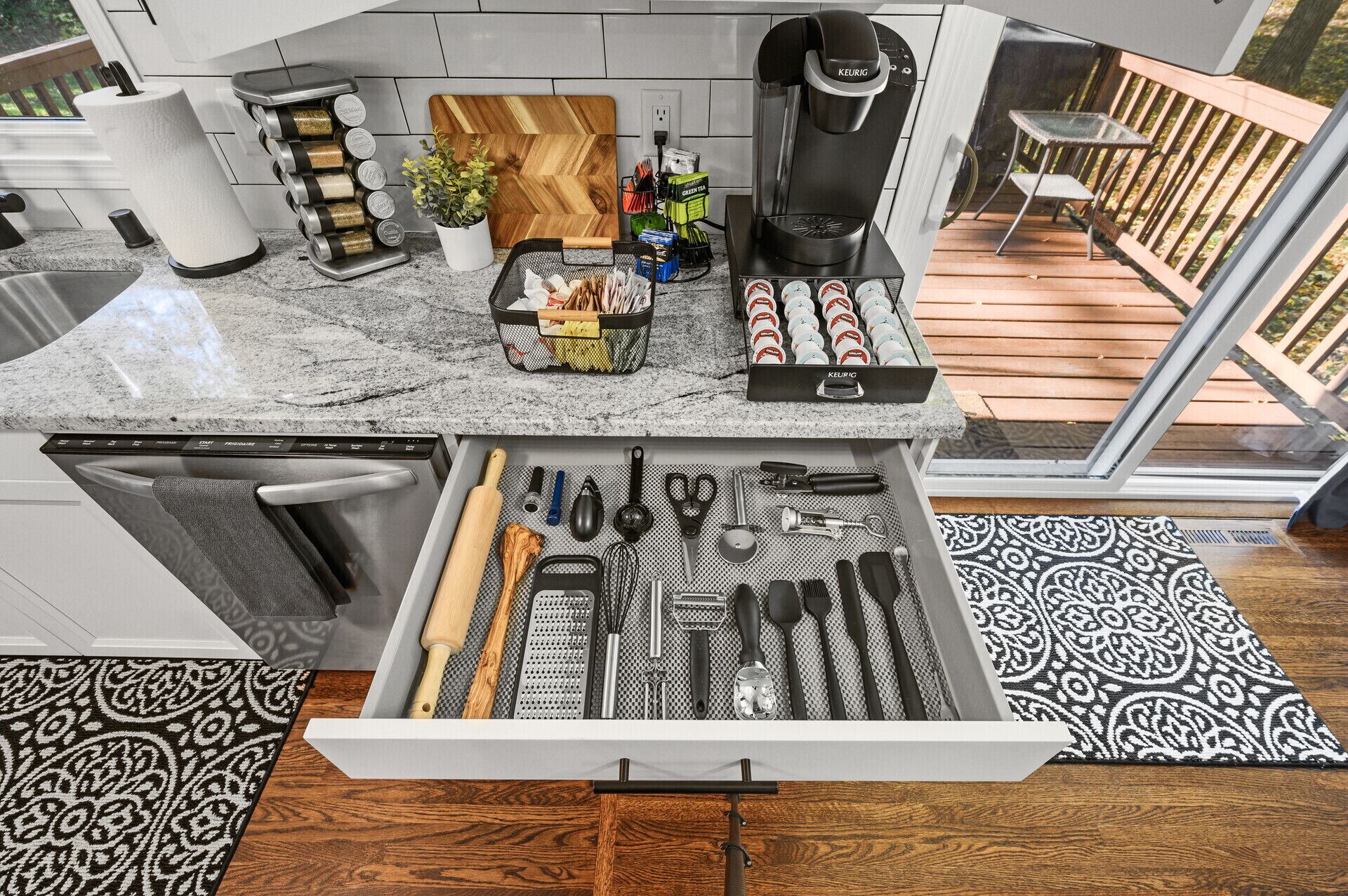 A kitchen with a built-in coffee maker, a variety of utensils in a drawer, and a wooden cutting board on the counter.