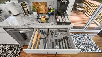 A kitchen with a built-in coffee maker, a variety of utensils in a drawer, and a wooden cutting board on the counter.