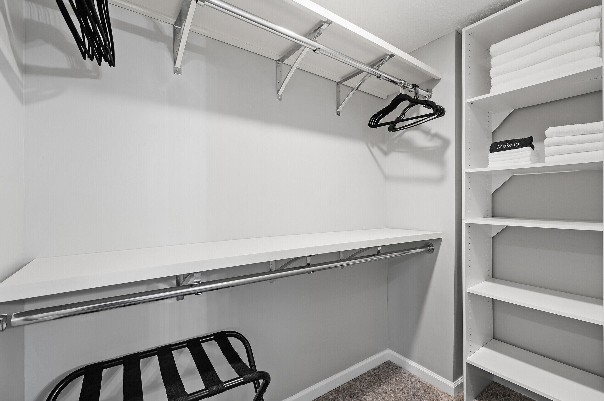 A walk-in closet with open shelving, a hanging rod, and a bench.