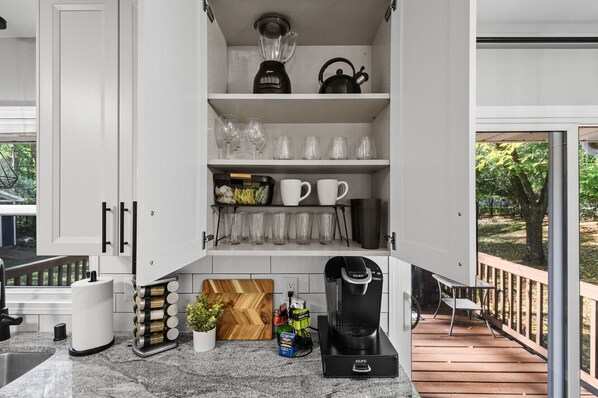 A kitchen with a built-in coffee maker, a blender, and a kettle on the shelves.