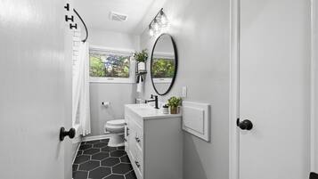 A bathroom with a toilet, sink, mirror, and shower.