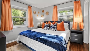 Une chambre à coucher avec un lit, deux tables de chevet, une commode et une fenêtre avec des rideaux.