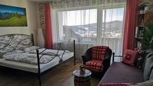 A cozy room with a bed, a sofa, a chair, and a small table. - One-room vacation apartment in vacation park with swimming pool (Missen-Wilhams)