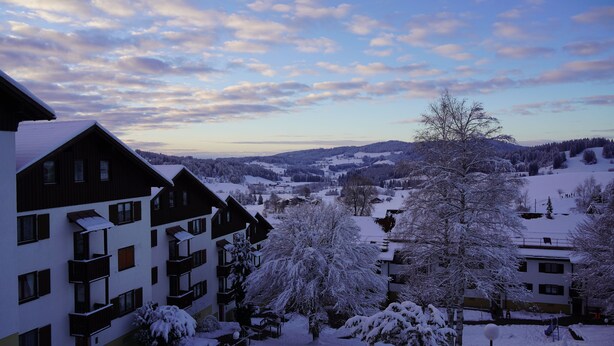 A snow-covered residential area with multi-story buildings, a clear sky, and a distant view of a valley. - One-room vacation apartment in vacation park with swimming pool (Missen-Wilhams)